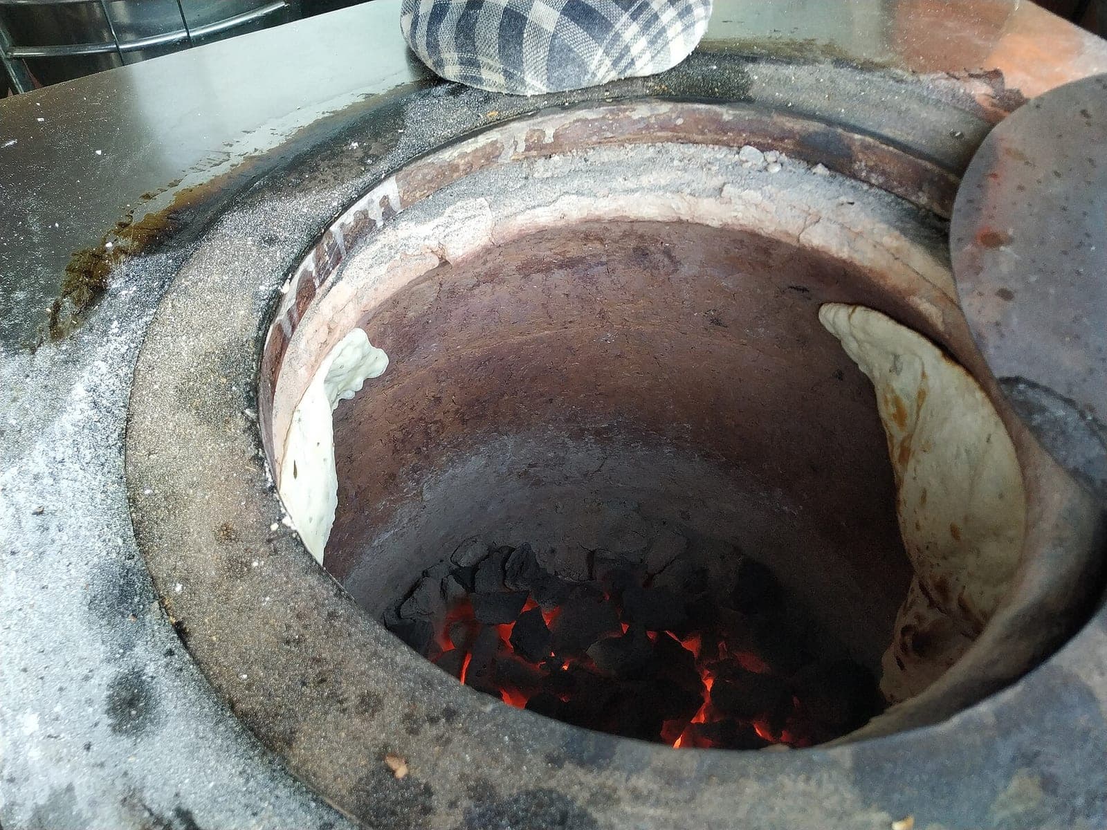 Naan baking over glowing coals inside a tandoor